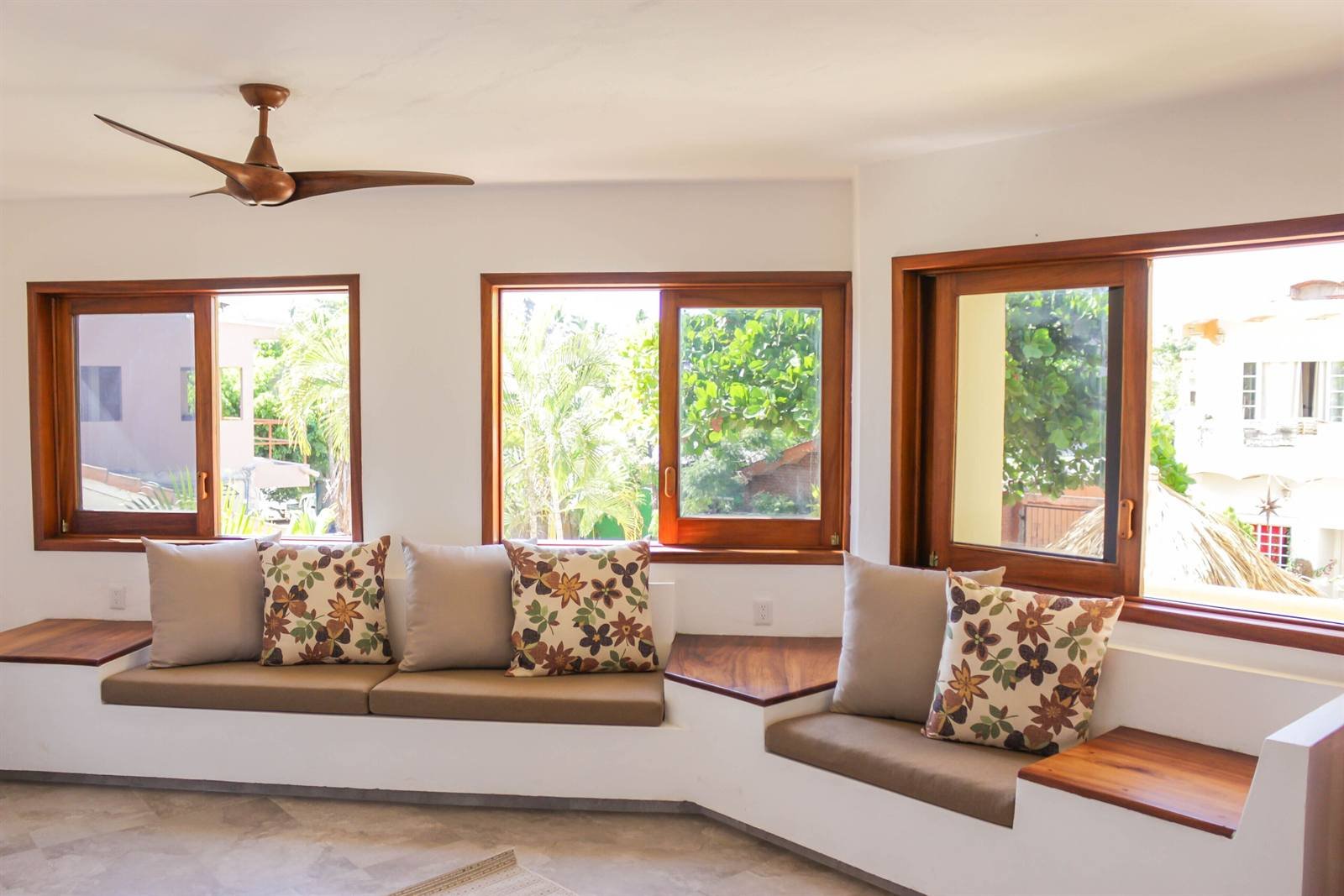 Casa Di Giulio: bright lounge with built-in cushioned benches and wood-framed windows onto the trees